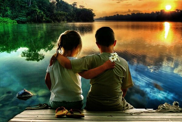 Ragazzo e ragazza abbracciati sulla riva del fiume e guardando il tramonto