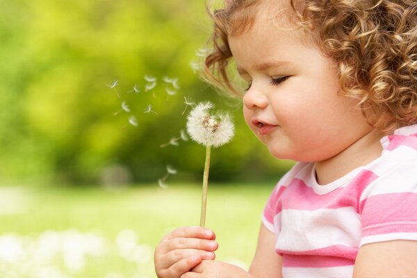 Bambina che soffia sui denti di leone