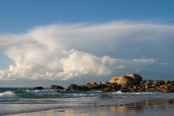 Onde sulla riva sabbiosa contro le nuvole